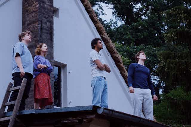 Four people stand on a roof, looking at the sky.