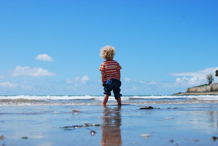 Child stands in water, pants pulled up to the knees