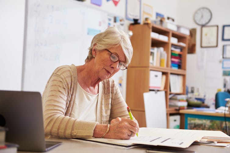 A teacher writes in a book, sitting at her desk.