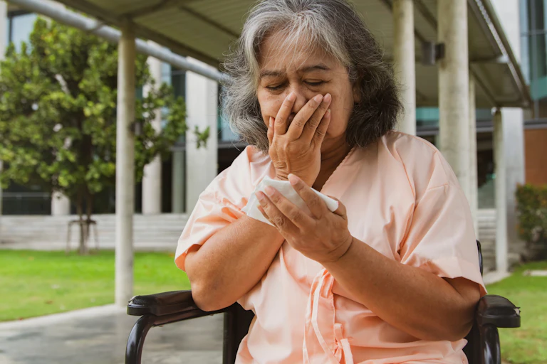 woman sits outside, covers mouth, holds tissue