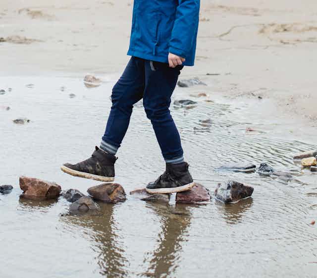 Children walking across stones on a beach.