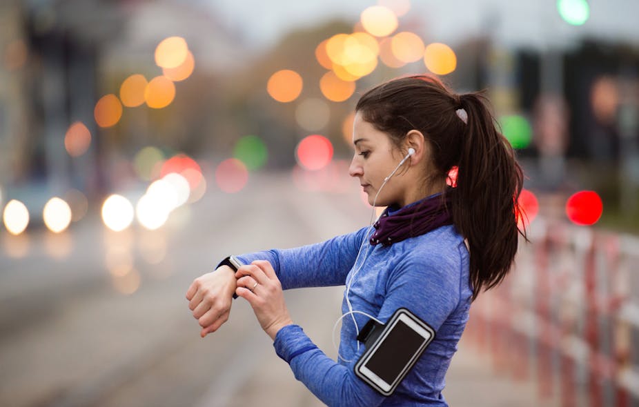 Jeune femme en sweat-shirt bleu courant dans la ville et regardant sa montre connectée