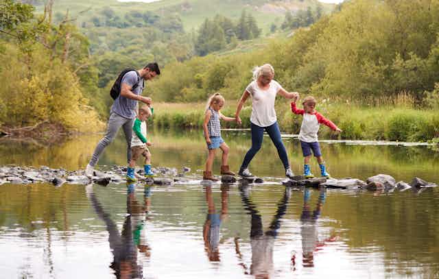 Two parents and three children walk over stones in a stream.