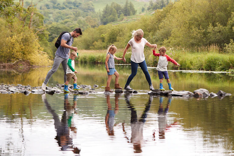Two parents and three children walk over stones in a stream.
