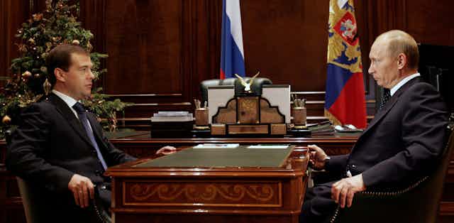 Then Russian president Dmitry Medvedev sits opposite his predecessor and successor Vladimir Putin at a desk in the Kremlin