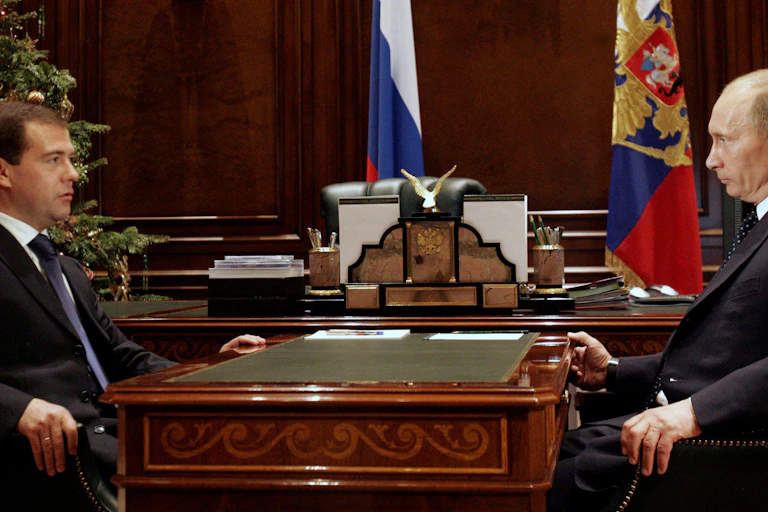 Then Russian president Dmitry Medvedev sits opposite his predecessor and successor Vladimir Putin at a desk in the Kremlin