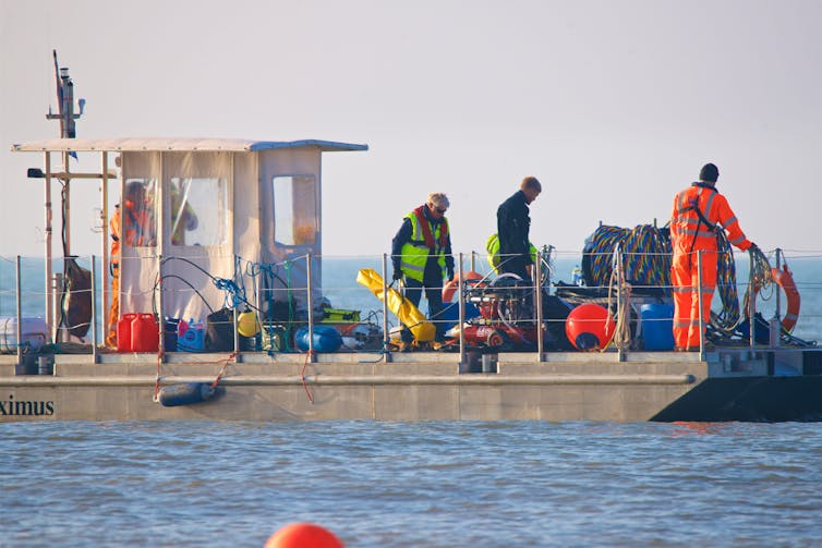 Men stand on the deck of a boat feeding cable into the sea.