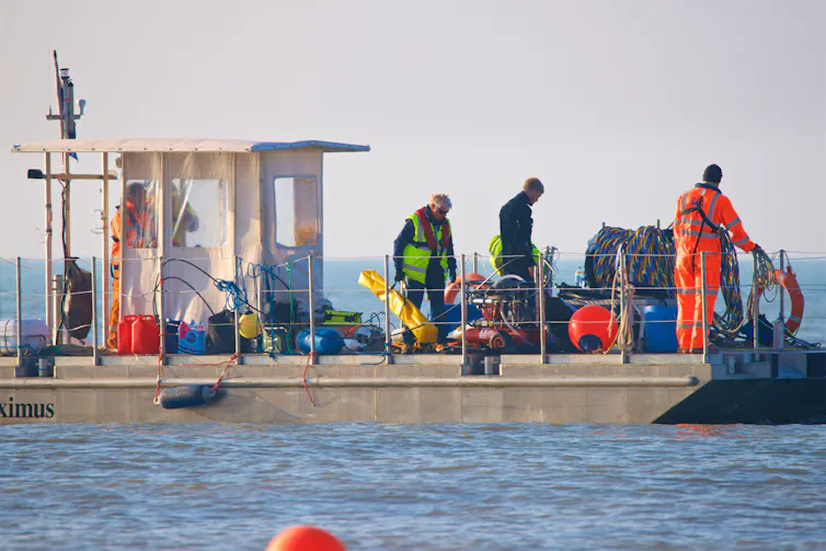 Men stand on the deck of a boat feeding cable into the sea.