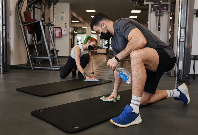 Deux personnes sont en train de passer des produits sur des tapis de sol au milieu d’une salle de fitness