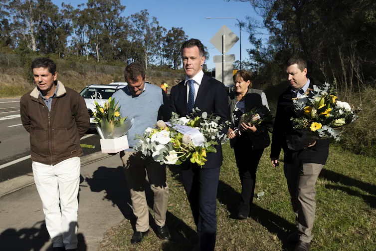 People walking near roadside carrying flower bouquets