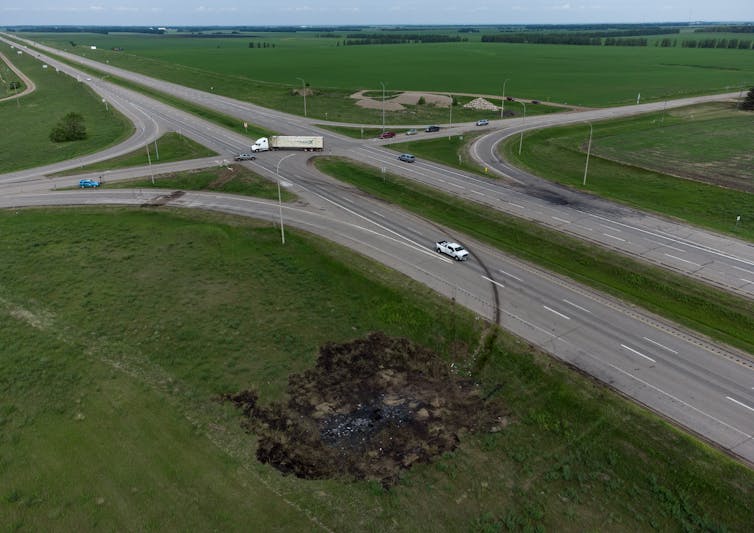 A scorched patch of ground near a highway intersection. Skid marks leading to the scorched patch are seen on the roadway.