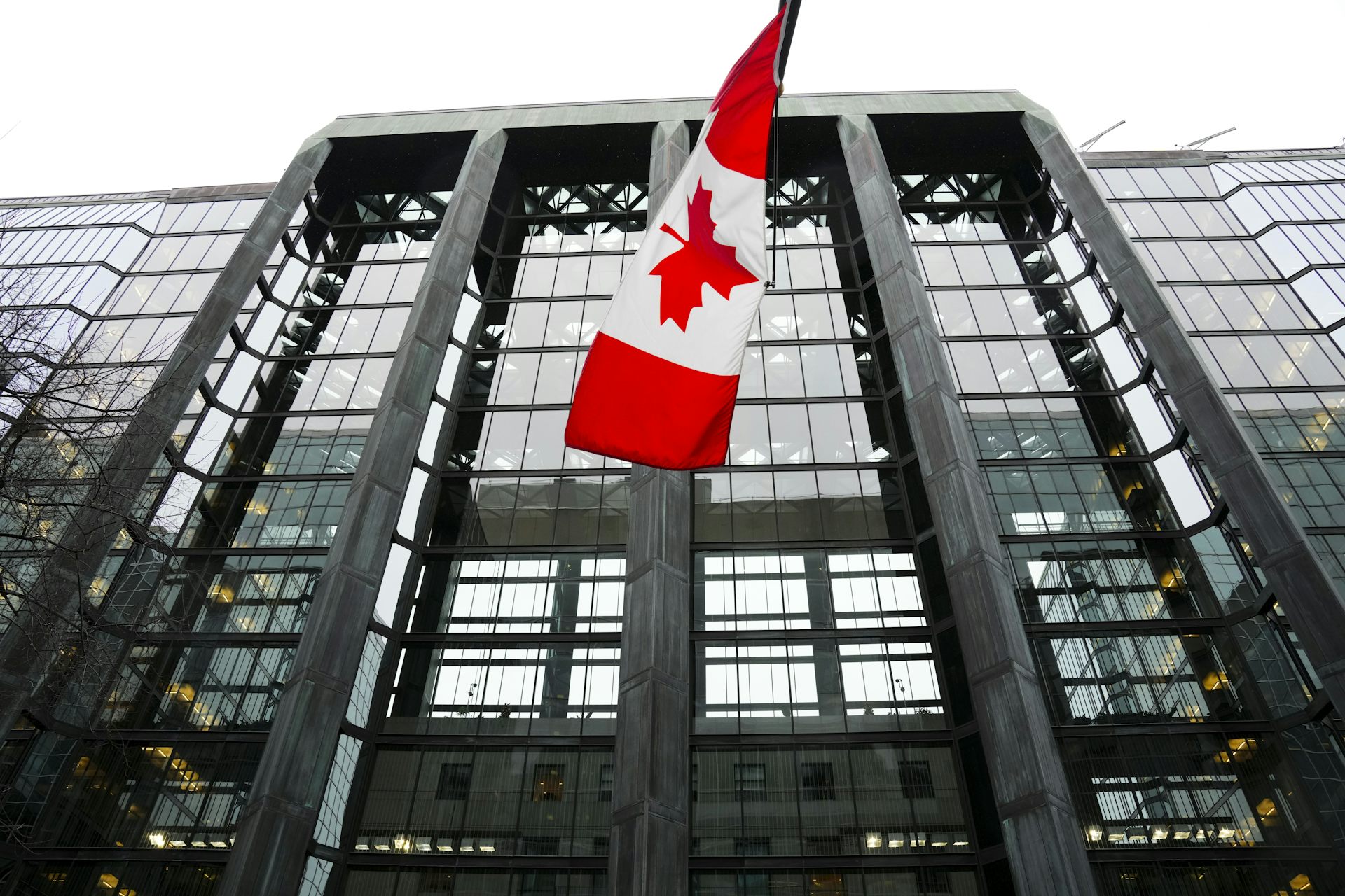 A Canadian flag hangs from the front of a glass-fronted office building.