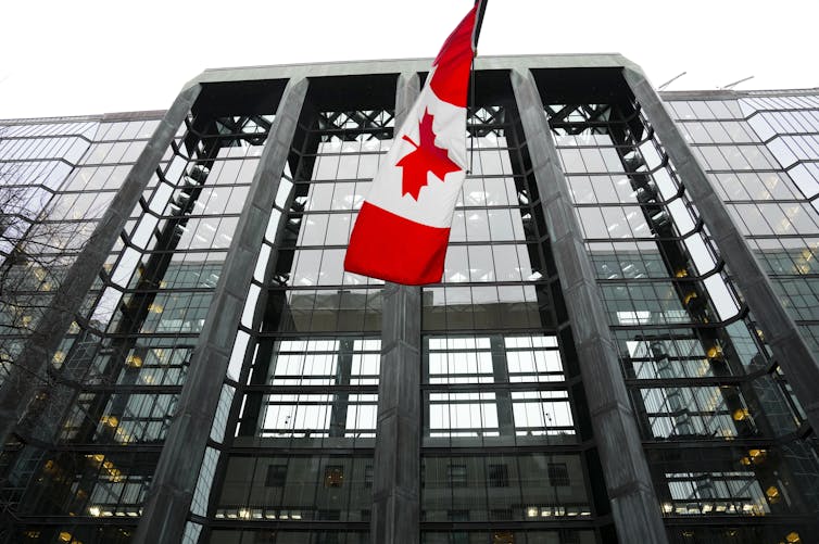 A Canadian flag hangs from the front of a glass-fronted office building.
