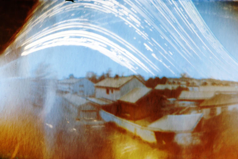 A somewhat blurry photo of a landscape of houses with curved white lines traced in the sky.