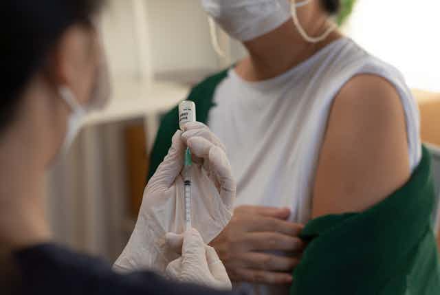 health worker holds syringe as patient exposes upper arm