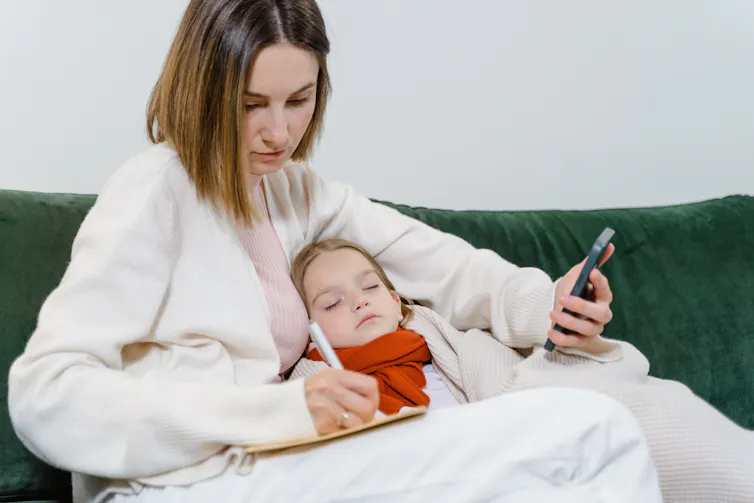 A mother works while a child sleeps under her arm.