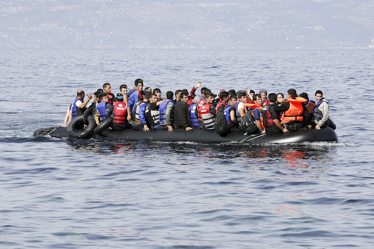 A group of people wearing life jackets while on a lifeboat in the middle of a large body of water