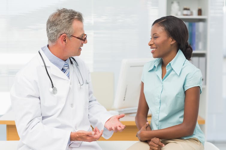 A young woman speaks to her older male doctor.