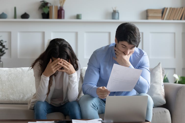 شاب وامرأة يجلسان على الأريكة ويبدو عليهما التوتر. إنه ينظر إلى وثيقة ورأسها بين يديها.