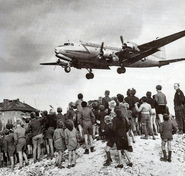 A plane flies over the heads of a crowd of people during the Berlin airlift.