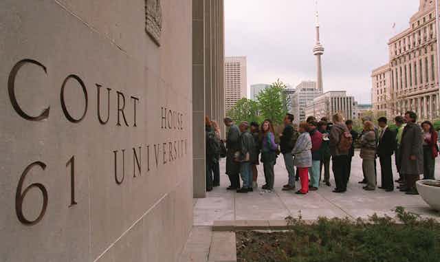 People line up outside a courthouse. The CN Tower is in the background.