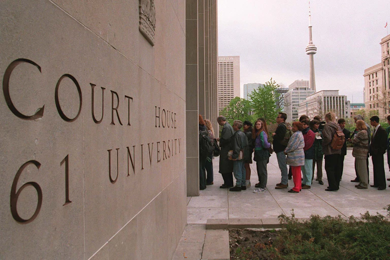 People line up outside a courthouse. The CN Tower is in the background.
