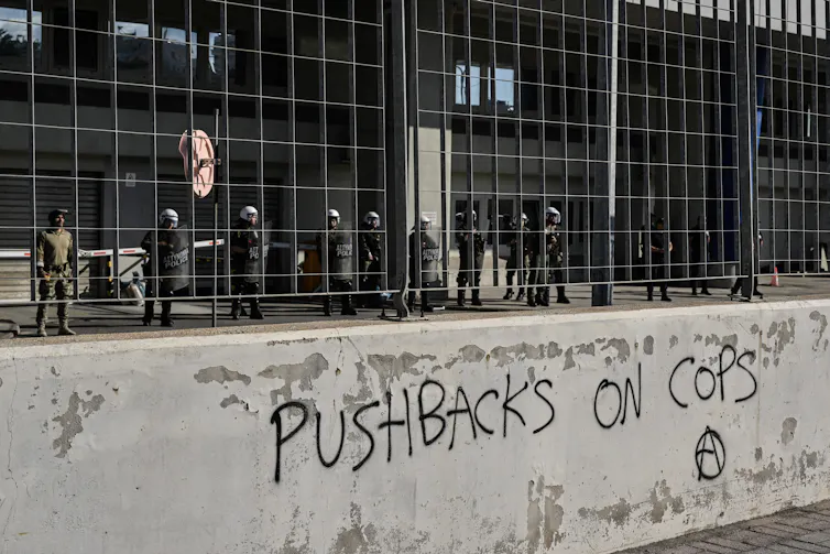 Des policiers protègent le quartier général de Frontex et des garde-côtes helléniques dans le port du Pirée, près d’Athènes, le 18 juin 2023, lors d’une manifestation contre les politiques de l’UE et du gouvernement grec à la suite du naufrage d’un bateau