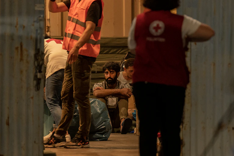 Un survivant d'un naufrage est assis dans un entrepôt à côté du personnel médical dans le port de la ville de Kalamata, le 14 juin 2023, après le naufrage d'un bateau transportant des dizaines de migrants dans les eaux internationales de la mer Ionienne.