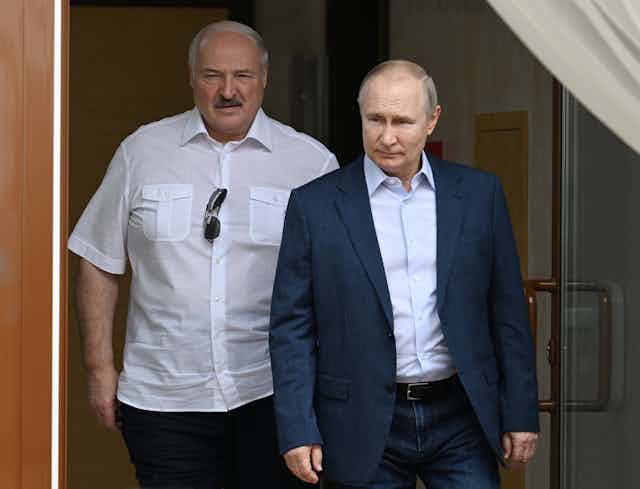 Vladimir Putin in a jacket walks in front of Belarus president Alexander Lukashenko.