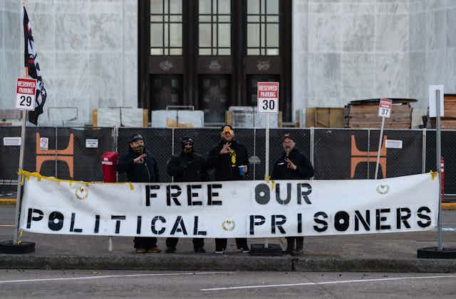 Four men in front of a large building holding a banner that says 'Free our political prisoners'