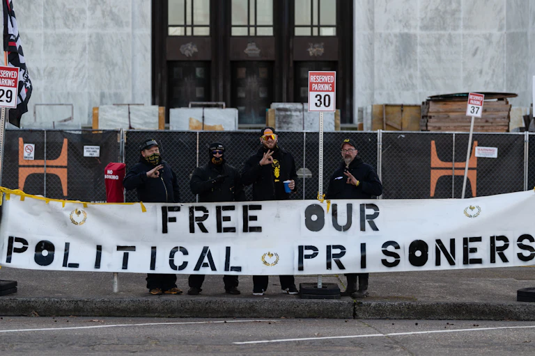 Four men in front of a large building holding a banner that says 'Free our political prisoners'