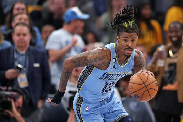 Man with dreadlocks in blue jersey dribbling basketball.