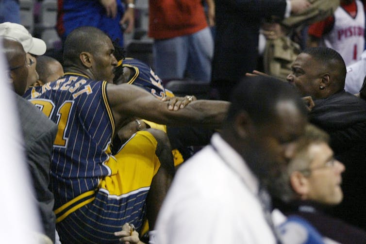 Basketball fan grabbing arm and tusseling with basketball player.