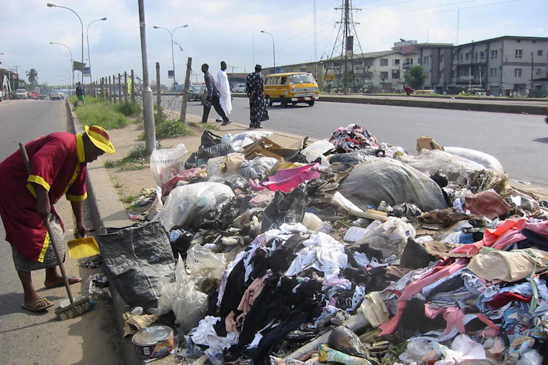 Woman sweeping the highway near a heap of rubbish.