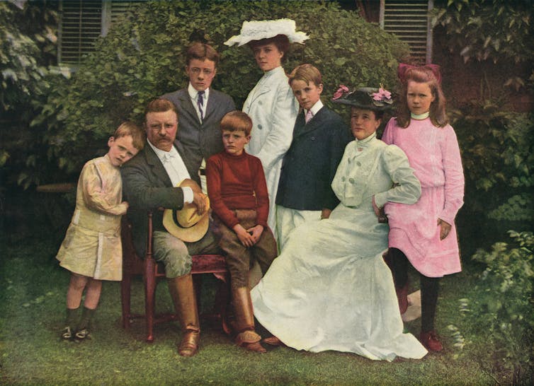 A family photo shows a man and a woman seated, surrounded by six children ranging in age from toddler to teen.