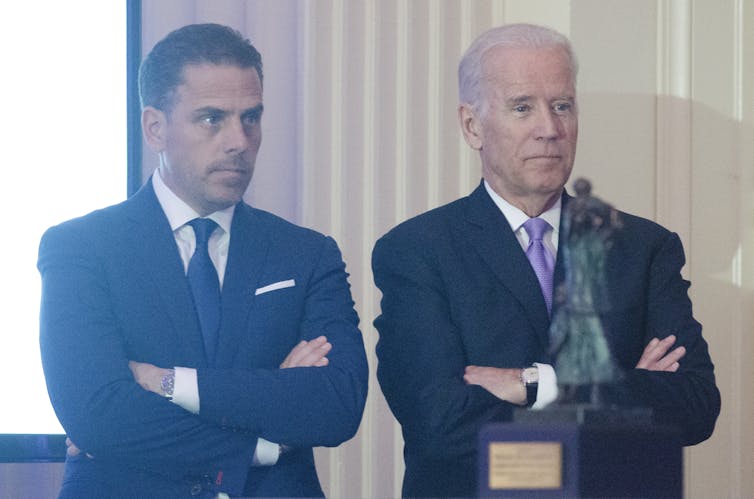 Hunter Biden y Joe Biden, ambos vestidos de traje, están uno al lado del otro, con los brazos cruzados.