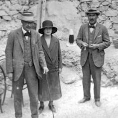Dos hombres y una mujer ante la entrada de las piedras de una tumba egipcia.