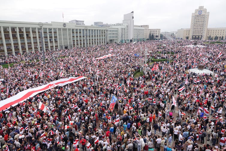 A huge crowd of people holding Belarusian flags and colors.