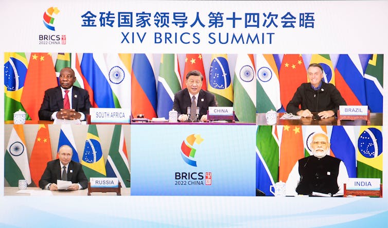 Under a banner with Chinese letter and 'XIV BRICS SUMMIT' five screens show the face of five world leaders in front of flags.