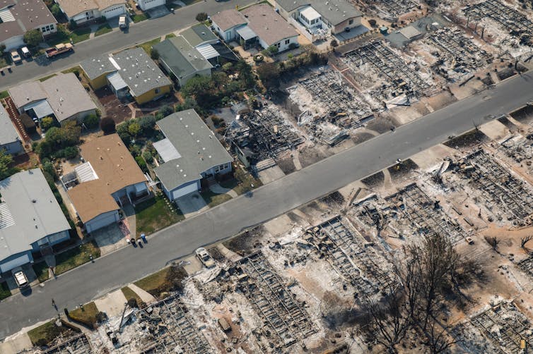 An aerial view of a community of small, closely built houses, with half the homes in the photo burned.