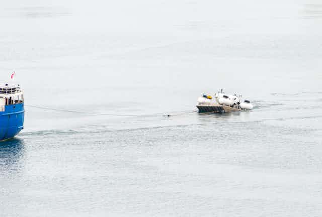 A large boat pulls a much smaller vessel on the open ocean