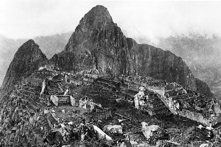Fotografía en blanco y negro de unas ruinas arqueológicas situadas en lo alto de una montaña.