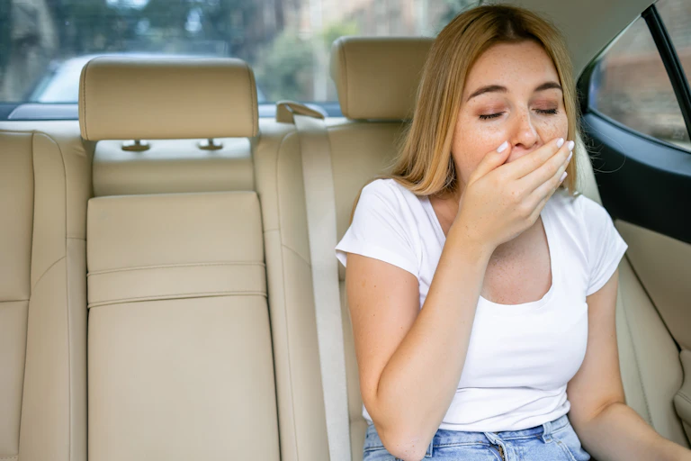 Une jeune femme est assise, nauséeuse, à l'arrière d'une voiture.