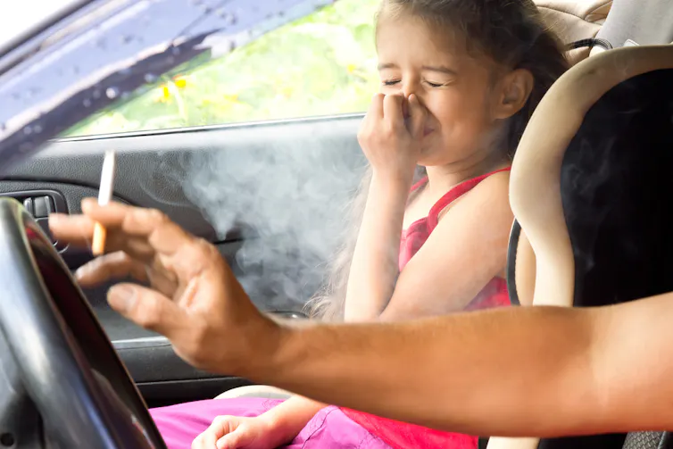 A little girl is bothered by cigarette smoke inside the car.