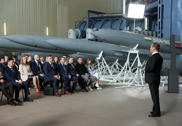 Dmitry Mevedev speaking to a seated audience in front of large missiles.