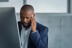 A man rubs his temple while wincing in pain
