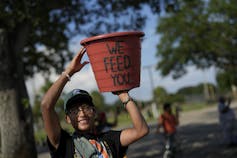 A Latino teen hoists a harvesting bucket market with the words