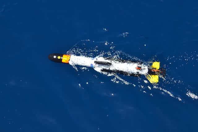a torpedo-shaped object moves just below the surface of the ocean