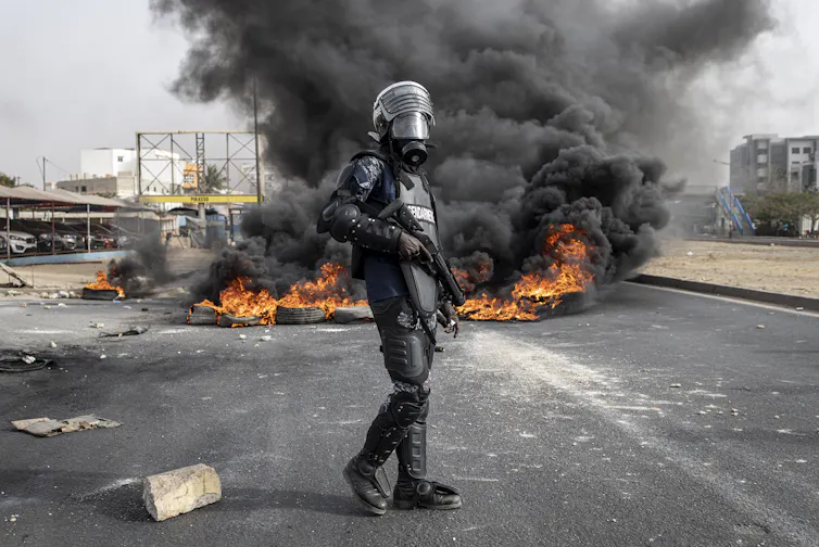 Policier séégalais devant i,e voiture en feu