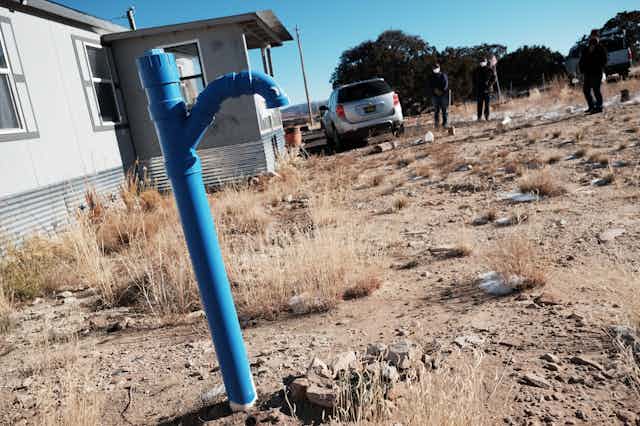 A blue metal pump set in dry ground outside a modest house.